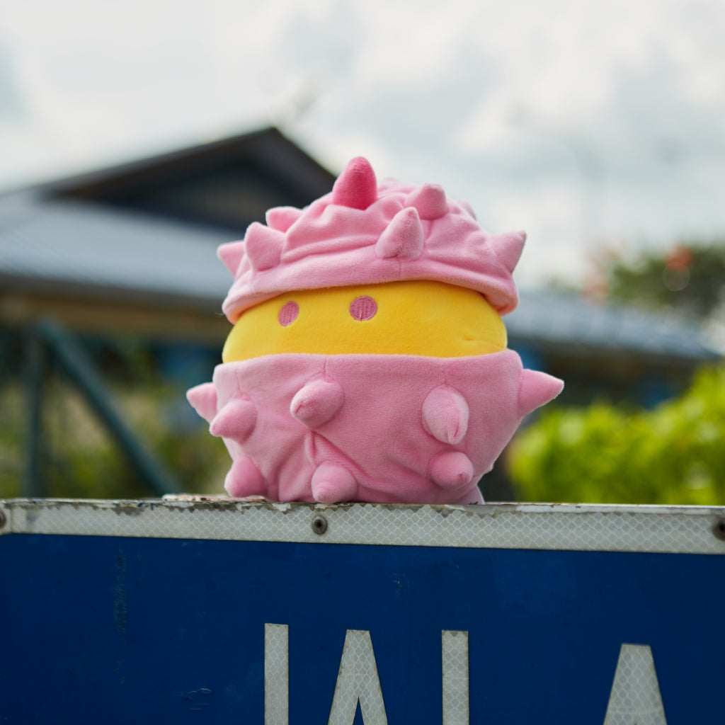 Pink and yellow Bella durian plushie photographed outdoors.
