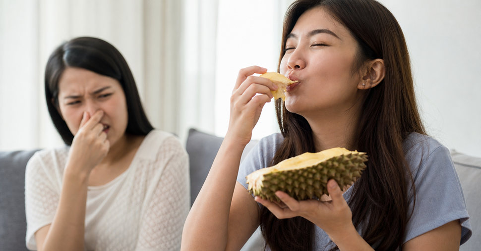 A woman enjoys eating durian, while another person covers their nose