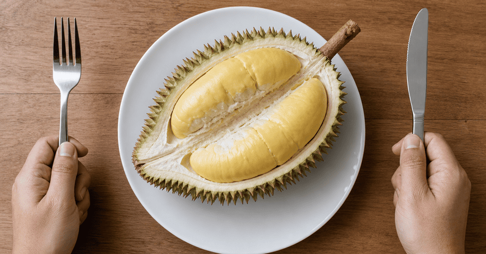 Hands holding knife and fork and an opened durian on the plate